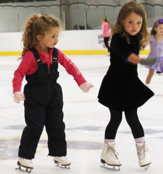 2 girls learning how to skate at beginner ice skating lessons.