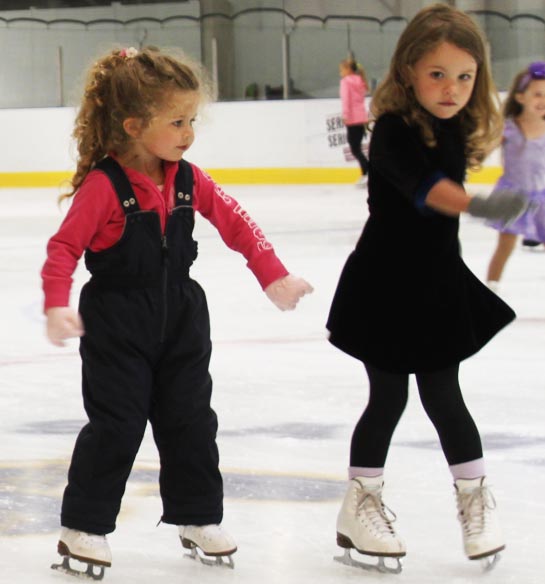 Curly-hair-sisters-in-ice-skating-lessons-opt 2 girls learning how to skate at beginner ice skating lessons.
