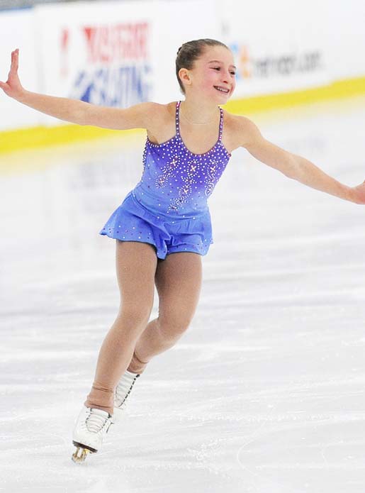 A skater in a purple dress practicing a routine during ice skating lessons.