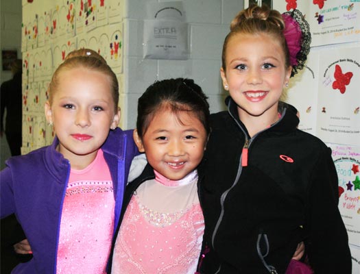 Three young figure skaters in full make-up ready to compete in the basic skills ice skating competition.