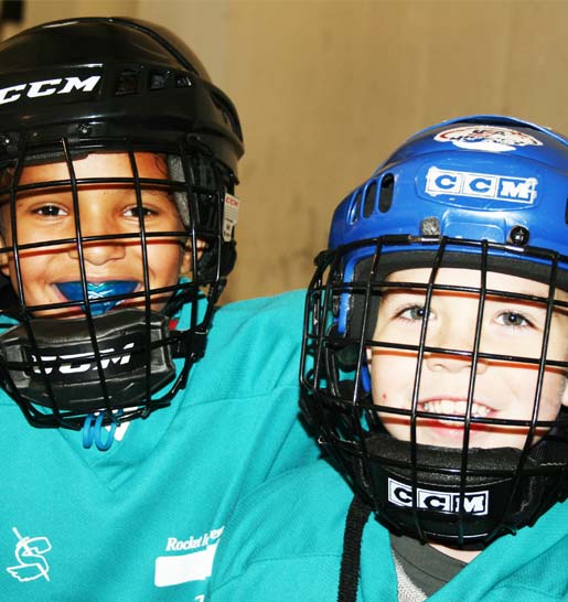 Two friends from hockey lessons smile for the camera in their hockey helmets