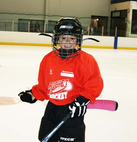 Young skater at hockey lessons smiling with hockey stick